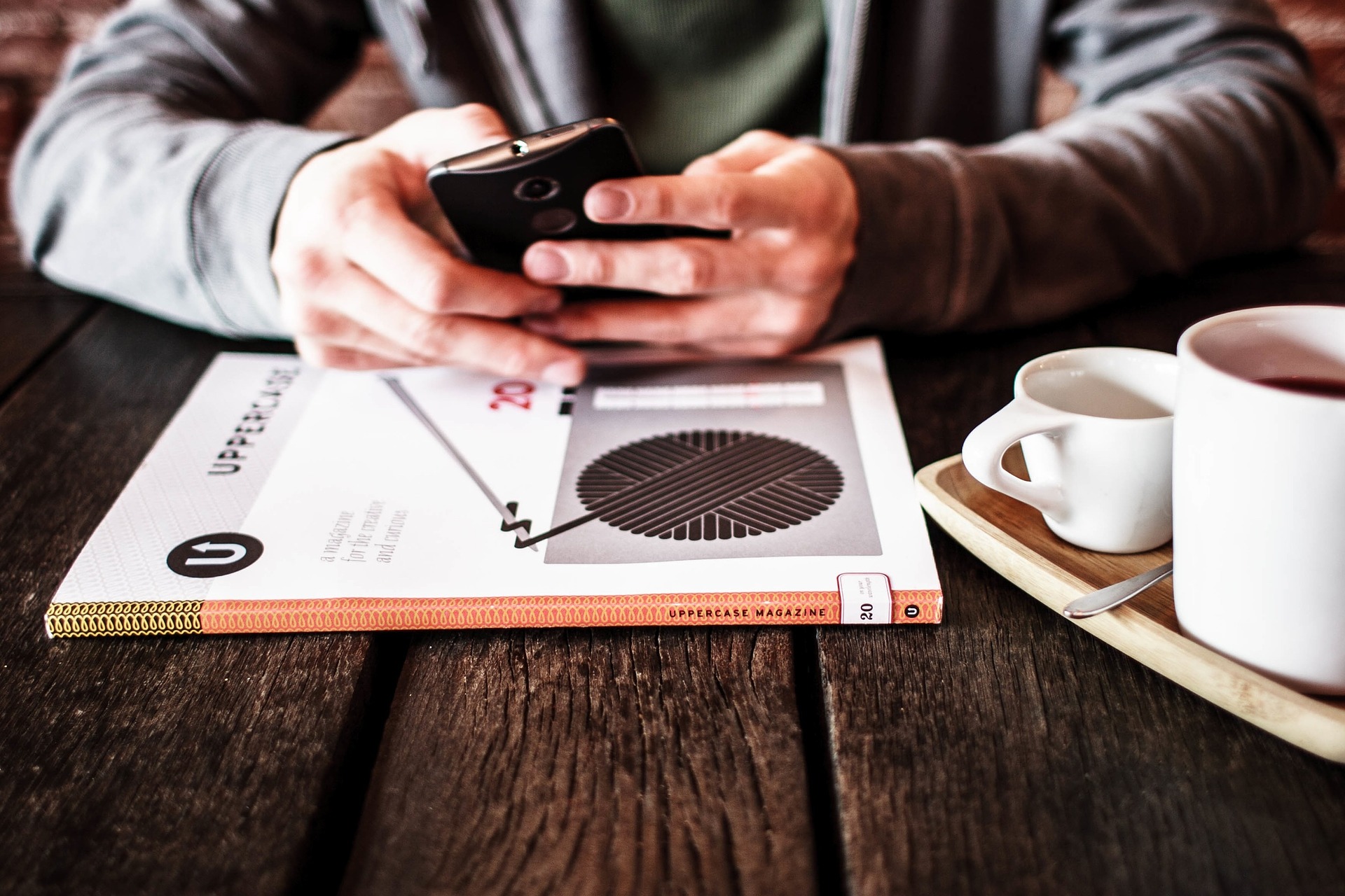 Mann liest am Smartphone mit Kaffee und Magazin